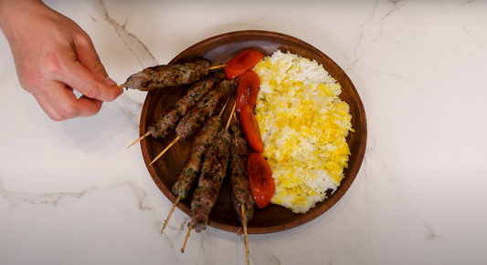 Grilled lamb chops and kofta skewers served with rice and vegetables on a white plate